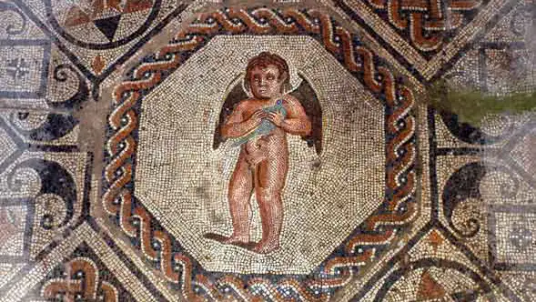 Mosaico romano da Casa do Mitreo em Mérida com figura de cupido alado no centro, rodeado de padrões geométricos e entrelaçados em pedras coloridas