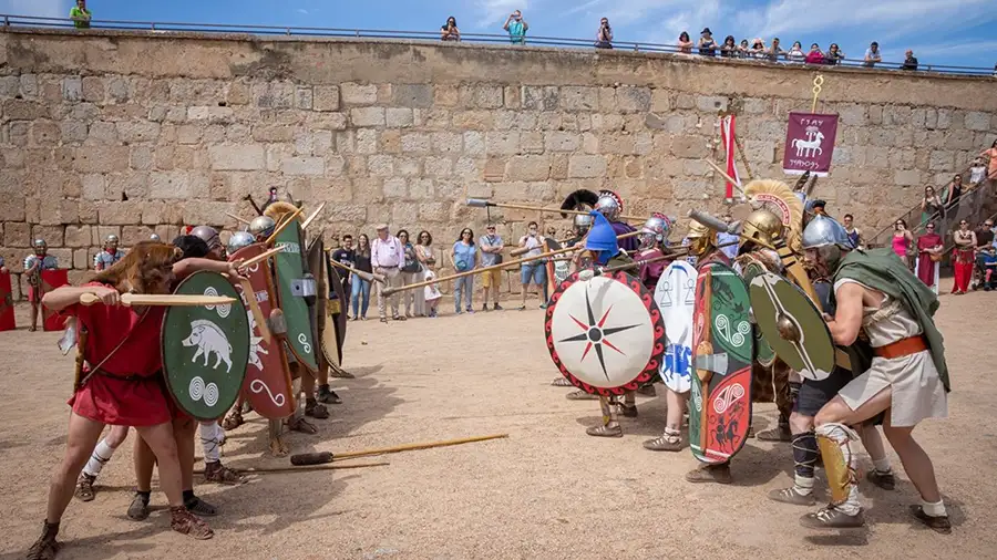 Recreação de combate de gladiadores durante o festival Emerita Lvdica em Mérida, com participantes em trajes e armaduras romanas e público nas muralhas ao fundo