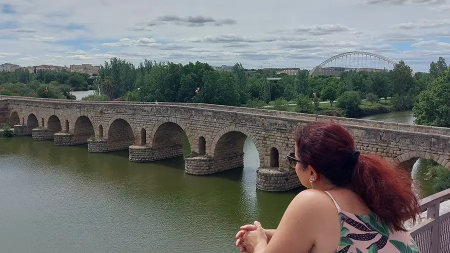 Mulher observando a Ponte Romana sobre o rio Guadiana em Mérida, com os arcos de pedra da ponte e a cidade ao fundo