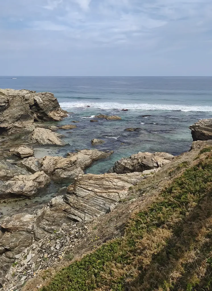 Vista aérea da costa rochosa da praia das Catedrais na Galícia, com água turquesa entre as pedras e o mar Cantábrico ao fundo