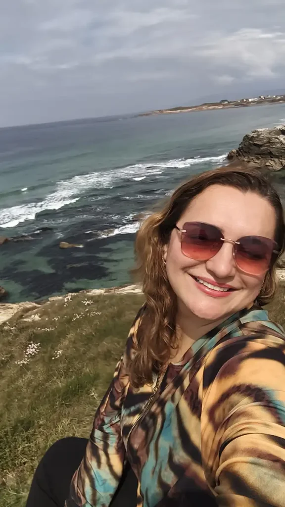 Mulher sorrindo com óculos de sol no mirador da praia das Catedrais com o mar Cantábrico e as rochas ao fundo