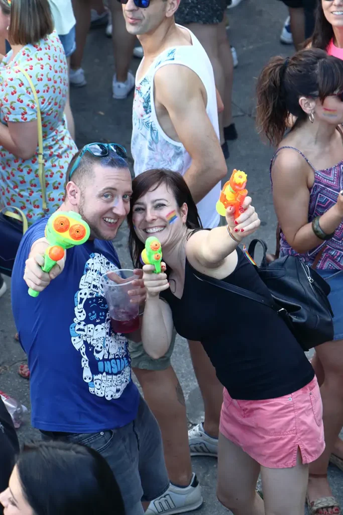 Casal sorridente segura pistolas de água e apontam para a câmera em meio à multidão durante o Orgulho de Madrid