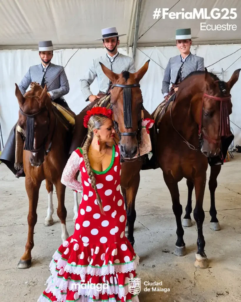 Mulher de vestido de flamenca vermelho de bolinhas brancas posa diante de três cavaleiros com trajes tradicionais e chapéus de aba larga na área equestre da Feria de Málaga