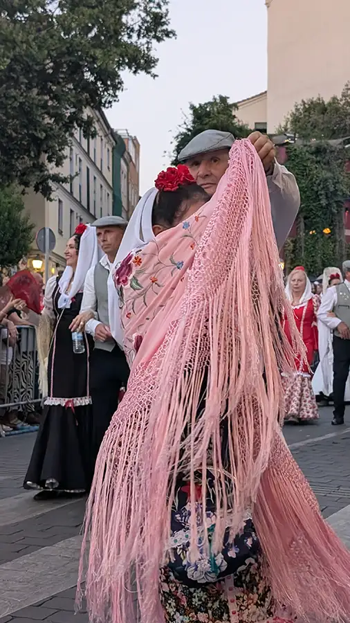 Pareja bailando el chotis madrileño, el hombre con boina y la mujer con un chal rosa bordado, durante las fiestas de agosto.