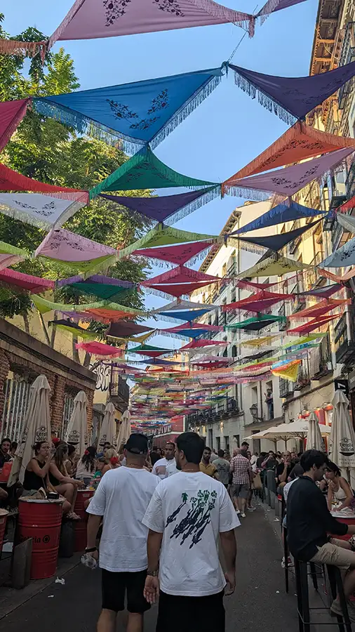 Chales de colores decorando las calles de Madrid durante las Fiestas de Agosto, vistos desde abajo formando un mosaico geométrico.