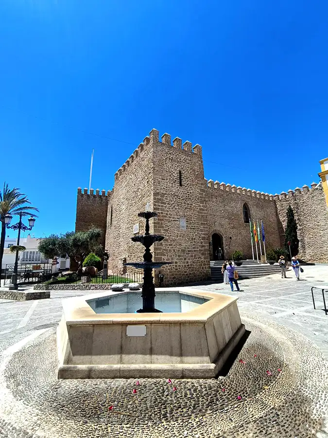 Fachada completa do Castillo de la Luna em Rota, com fonte na praça em frente