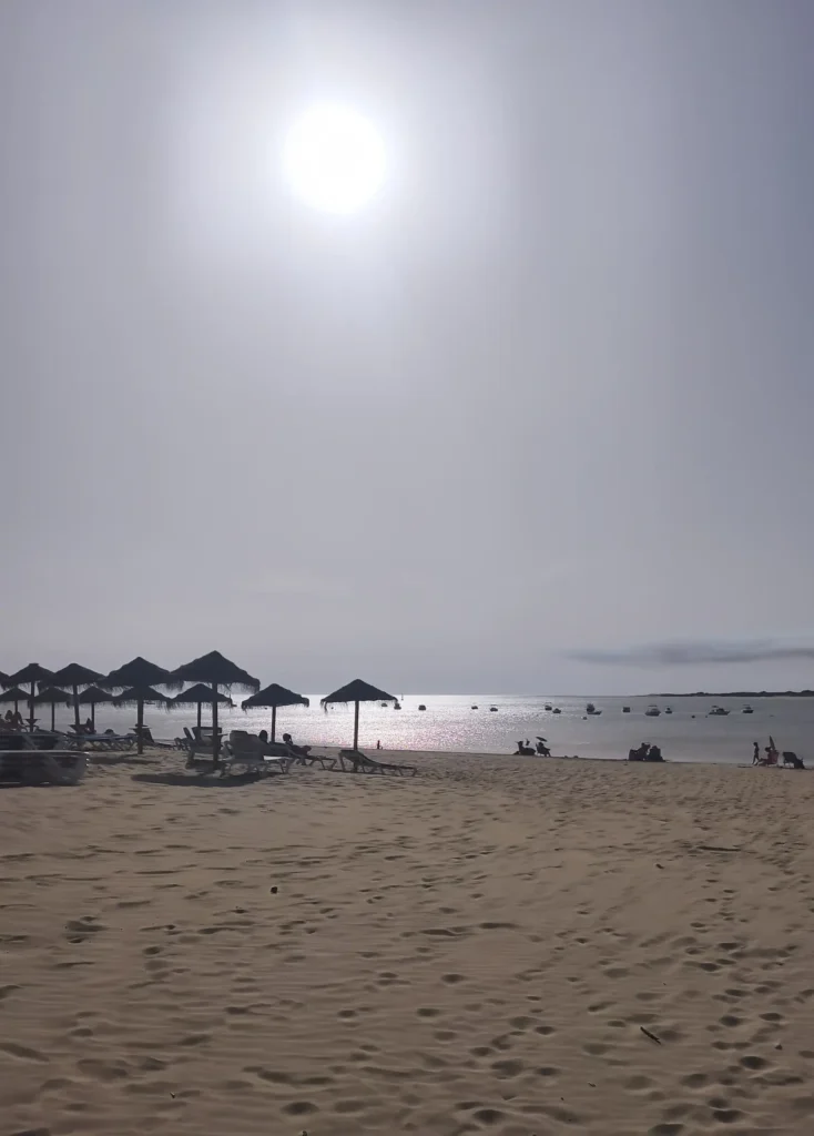 Praia de Sanlúcar de Barrameda ao entardecer, com sombrinhas de palha, cadeiras de praia e barcos ancorados na foz do Rio Guadalquivir