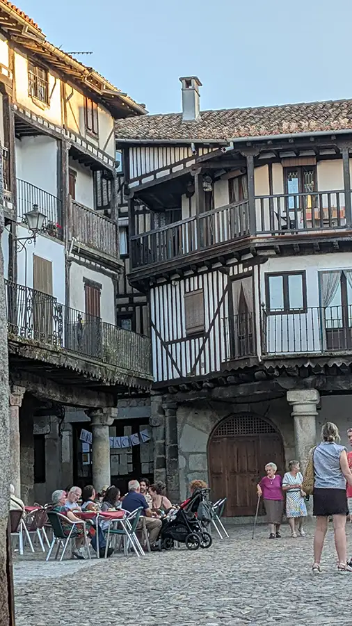 Casas típicas de pedra e entramado de madeira na Plaza Mayor de La Alberca, Salamanca, com pessoas sentadas em um bar ao ar livre