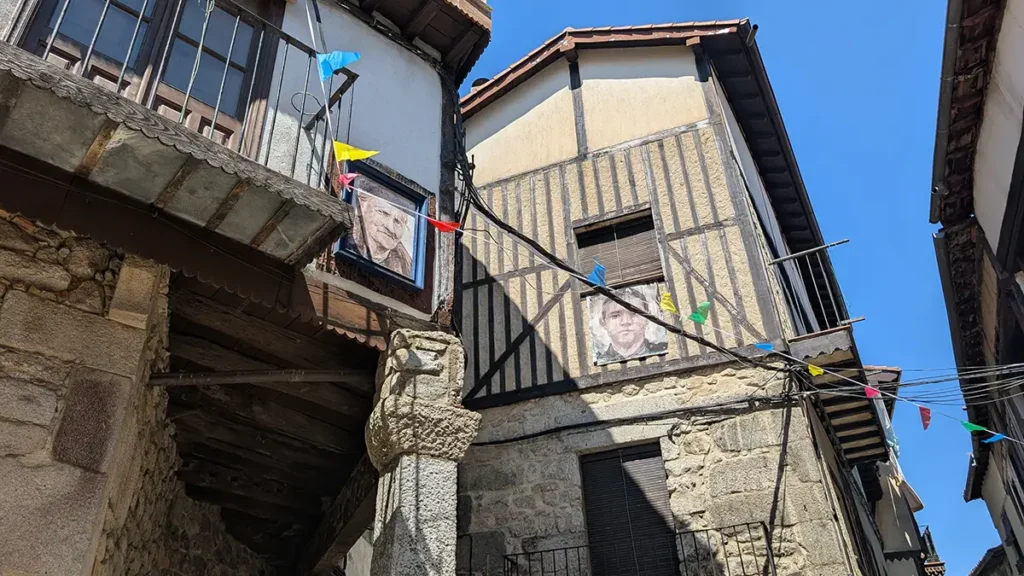 Casas de pedra e madeira em rua de Mogarraz com retratos de moradores nas paredes.