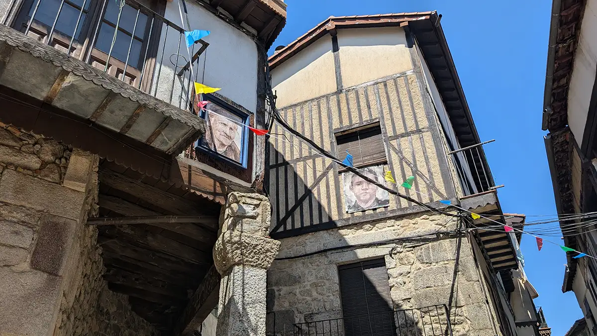 Casas de pedra e madeira em rua de Mogarraz com retratos de moradores nas paredes.