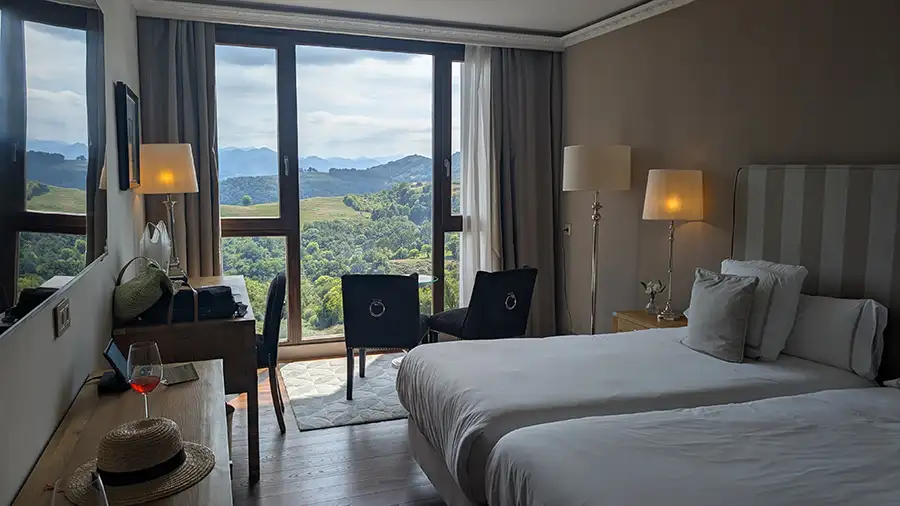 Quarto do Puebloastur com duas camas e janela do chão ao teto com vista para o vale e as montanhas