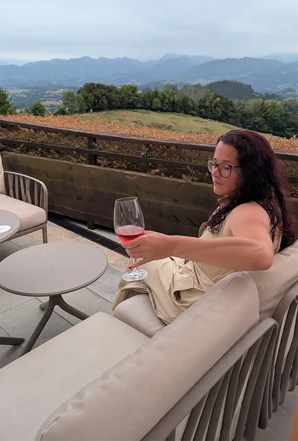 Mulher com taça de vinho na varanda externa da cafeteria do Puebloastur com vista para o vale