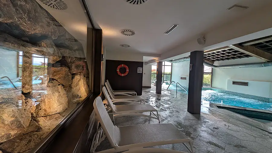 Área de descanso do spa do Puebloastur com espreguiçadeiras entre a piscina e a parede de pedra