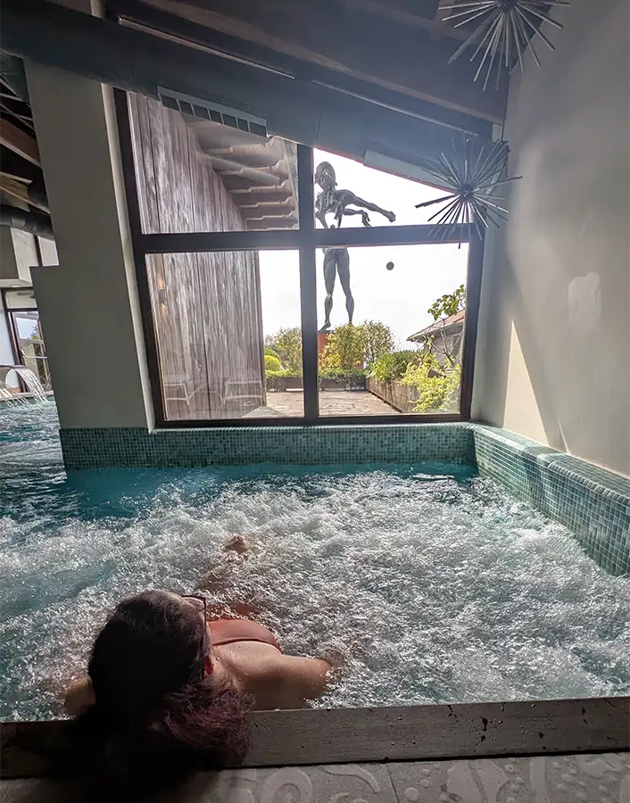 Mulher na piscina de hidromassagem do spa do Puebloastur com a escultura Newton de Dalí ao fundo