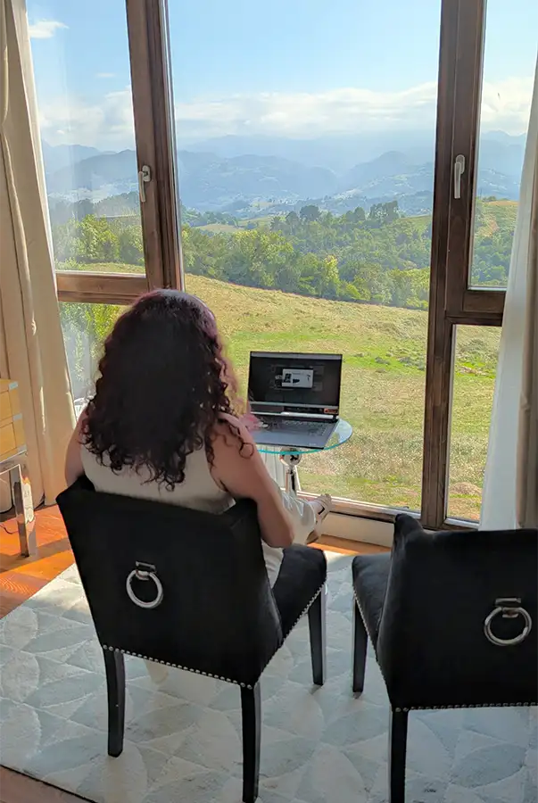 Mulher trabalhando no notebook diante da janela do quarto do Puebloastur com vista para o vale