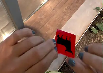 Mãos seguram um adesivo vermelho com a famosa silhueta preta do touro da Osborne.