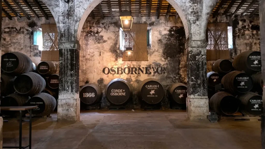 Sala de envelhecimento na bodega Osborne com barris de xerez empilhados sob arcos rústicos de pedra.