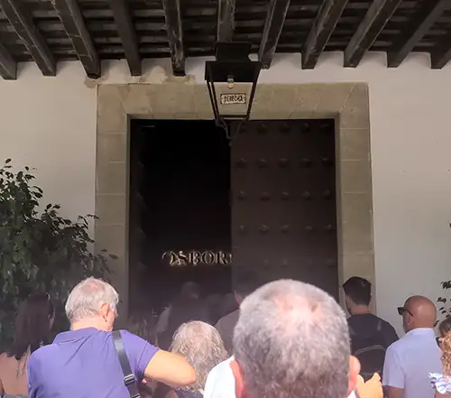 Turistas entram na adega Osborne através de um grande portão rústico de madeira.
