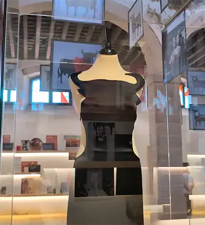 Vestido preto com decote em forma de chifres de touro exposto num manequim dentro de uma vitrine de vidro na galeria.