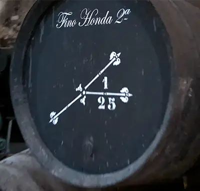 Detalhe de um barril de vinho escuro com inscrições a giz branco incluindo as palavras Fino Honda e números.