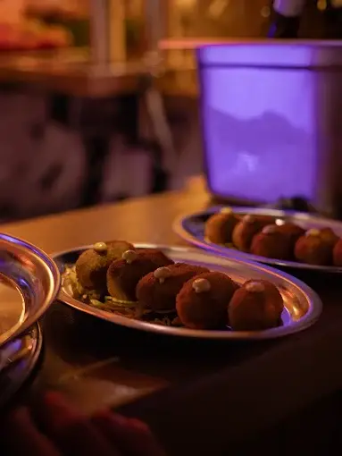 Dois pratos de inox com croquetes sobre o balcão, em ambiente de luz baixa.