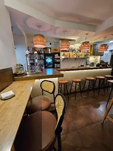 Interior do Cuarenta Bar de Vinos, com balcão claro, banquetas altas, luminárias de palha e prateleiras com garrafas ao fundo.