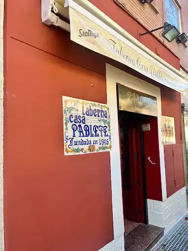 Fachada vermelha da taberna Casa Pablete em Aranjuez, com placa de azulejos ao lado da porta e toldo com o nome do bar.