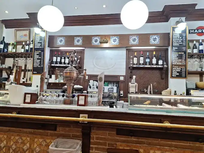 Barra da Casa Pablete com tiradores de chope em cobre, prateleiras de madeira com garrafas de vinho e quadros-negros com o cardápio de tapas ao fundo.