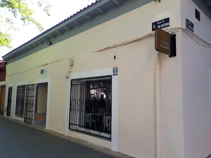 Fachada clara do Postas Tapería na esquina da Calle de San Antonio, com janelas de grade de ferro e placa de madeira na parede.