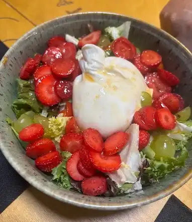 Salada de burrata com morangos fatiados, uvas verdes e folhas, servida em tigela de cerâmica.