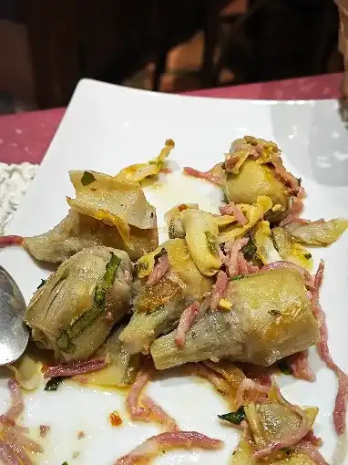 Prato branco com alcachofras salteadas e tiras de presunto, com um fio de azeite e ervas.