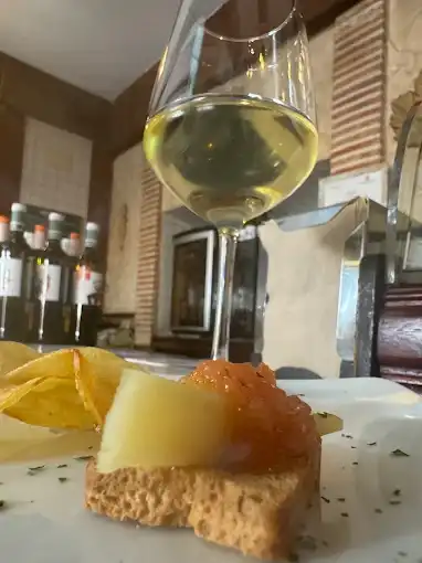 Taça de vinho branco ao fundo e, em primeiro plano, um prato com uma tosta com queijo e cobertura alaranjada, e batatas fritas ao lado.