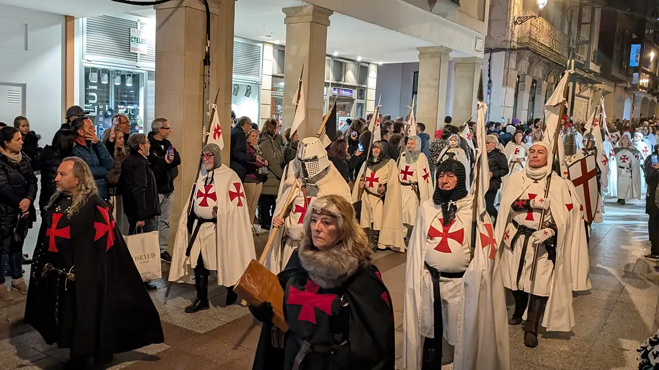 Pessoas vestindo trajes medievais de cavaleiros templários desfilam à noite por uma rua iluminada durante o Festival de las Ánimas em Soria enquanto o público assiste das calçadas.