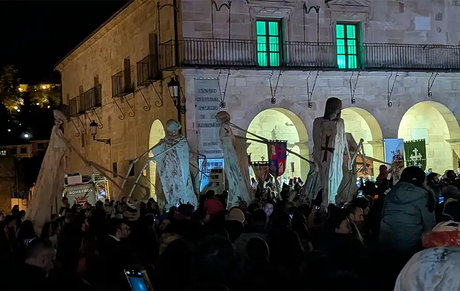 Representações gigantes de esqueletos passam em frente a um edifício de pedra iluminado numa praça de Soria.