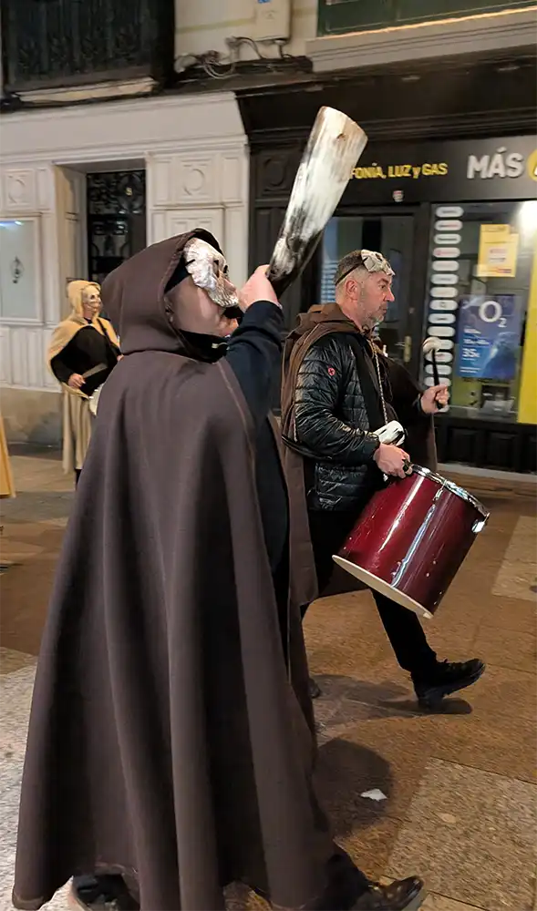Participantes encapuzados tocam um corno tradicional e um tambor nas ruas durante a celebração do festival