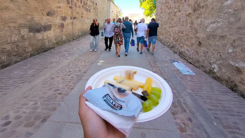 Prato de papel com queijos em cubos e uvas verdes numa rua de pedra de Zamora durante a feira do queijo