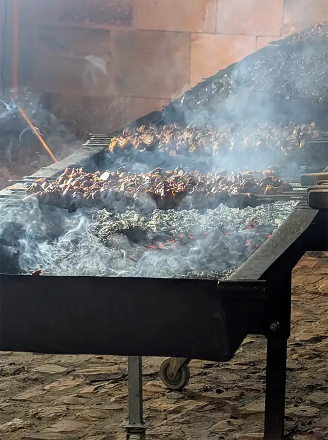 Espetos de carne grelhando na brasa, com fumaça, em grelha grande na feira do queijo de Zamora