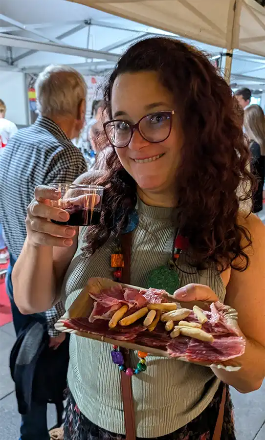 Mulher com copo de vinho tinto e bandeja de presunto curado com palitinhos de pão na feira do queijo de Zamora